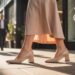 A confident city walker in stylish, supportive heels passes by professionals and a store sign promising relief for plantar fasciitis—showcasing fashionable comfort for busy urban lifestyles.