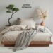A Japandi Bedroom styled with serene ideas boasts a low wooden bed adorned with beige bedding and a gray throw. A bonsai tree and pampas grass elevate the tranquil atmosphere. Walls feature pottery, while a wooden tray adds charm. Text reads JAPANDI BEDROOM.