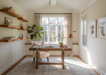 A cozy modern cottage office youll adore with a wooden desk and beige chair, large window with light curtains, potted plant, and wall-mounted wooden shelves. Inspiring minimalist decor and natural light create a soothing atmosphere.