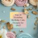 Colorful meringue swirls and flowers frame a note reading Top 10 Trending Birthday Cake Designs for 2025. The background is a soft blue with gold leaf accents.
