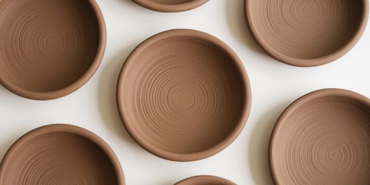 Several round, unpainted clay plates crafted from air-dry clay are arranged on a white surface. They have a smooth, professional finish with concentric circular patterns. The plates are positioned at various angles, creating a symmetrical and balanced composition.