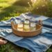 A sunlit picnic scene features a basket of lemonade jars atop a blue-and-white patchwork blanket, thoughtfully crafted from old jeans, set among flowers and sandals in the grass—celebrating creativity, sustainability, and the joys of summer outdoors.