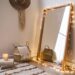 Transform your space with a cozy corner: a wood-framed full-length mirror adorned with string lights, complemented by woven baskets, candles atop stacked books, and stylish wall decor—making for an inspiring glow-up mirror setup.