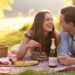 A joyful couple shares a romantic picnic amid lush greenery, savoring strawberries, cheese, and sparkling wine—capturing the essence of an idyllic summer date.
