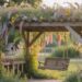 A wooden garden swing nestles beneath a pergola overflowing with vibrant wildflowers, while dappled sunlight and a nearby birdhouse complete the idyllic cottagecore scene.