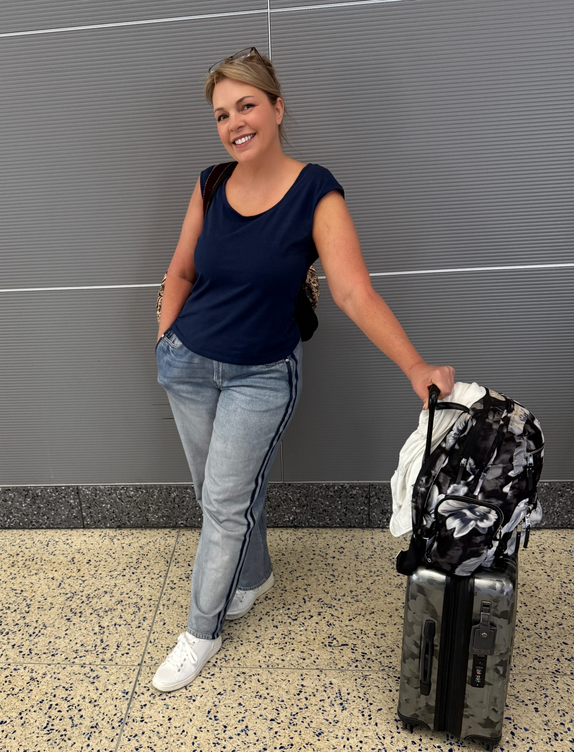 Ready for adventure, a smiling woman prepares to embark on a weeklong Alaska cruise, suitcase packed and travel essentials in hand.