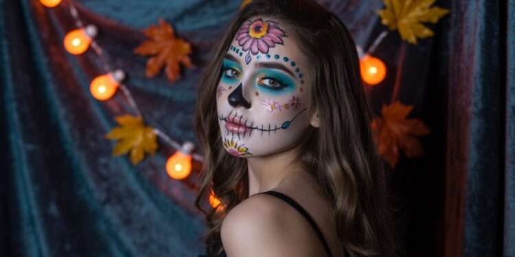 Día de los Muertos Makeup Inspiration: Woman with Colorful Face Paint, Autumn Leaves & Pumpkin Lights for Halloween Decor Ideas.