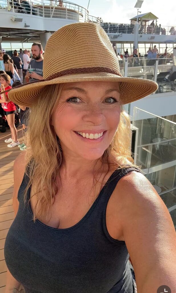 Smiling in a straw hat and black tank, a woman takes a sunny ship deck selfie on her lively tropical cruise. Product: IMG_2630.