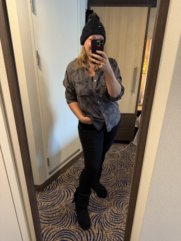 A mirror selfie showcases someone in a black beanie, gray rolled-sleeve shirt, black pants, and boots—cruise-ready style.