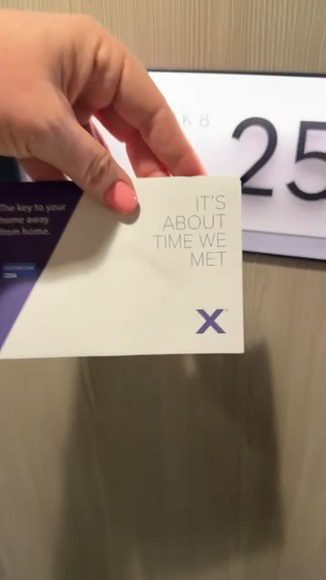 A pink-manicured hand displays an "ITS ABOUT TIME WE MET" card by cruise cabin 25, highlighting a fun cruise memory keepsake.