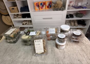 Assorted high-protein meals and snacks displayed on a beige cloth in a closet, with shelves stocked with shoes, hats, baskets, and blankets.