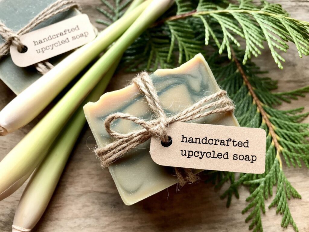 An artisanal soap bar made from recycled French fry grease rests on wood, adorned with twine, foliage, and lemongrass.