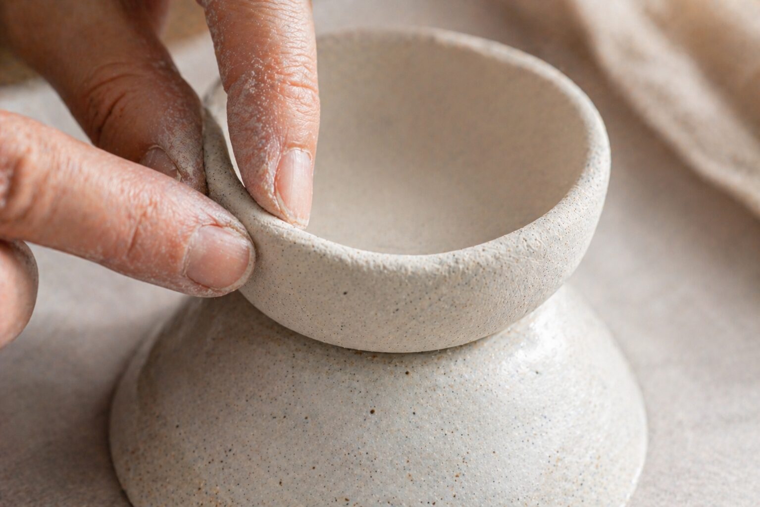 Close-up of fingers pinching the rim of a clay dish on an inverted bowl to even out the wall thickness