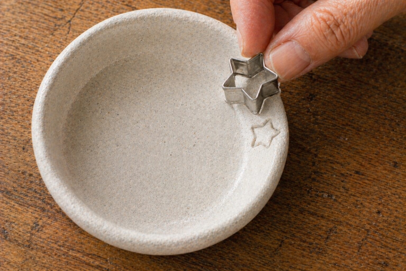 Small star-shaped cookie cutter pressed lightly into the soft clay rim of a dish to create a stamped impression
