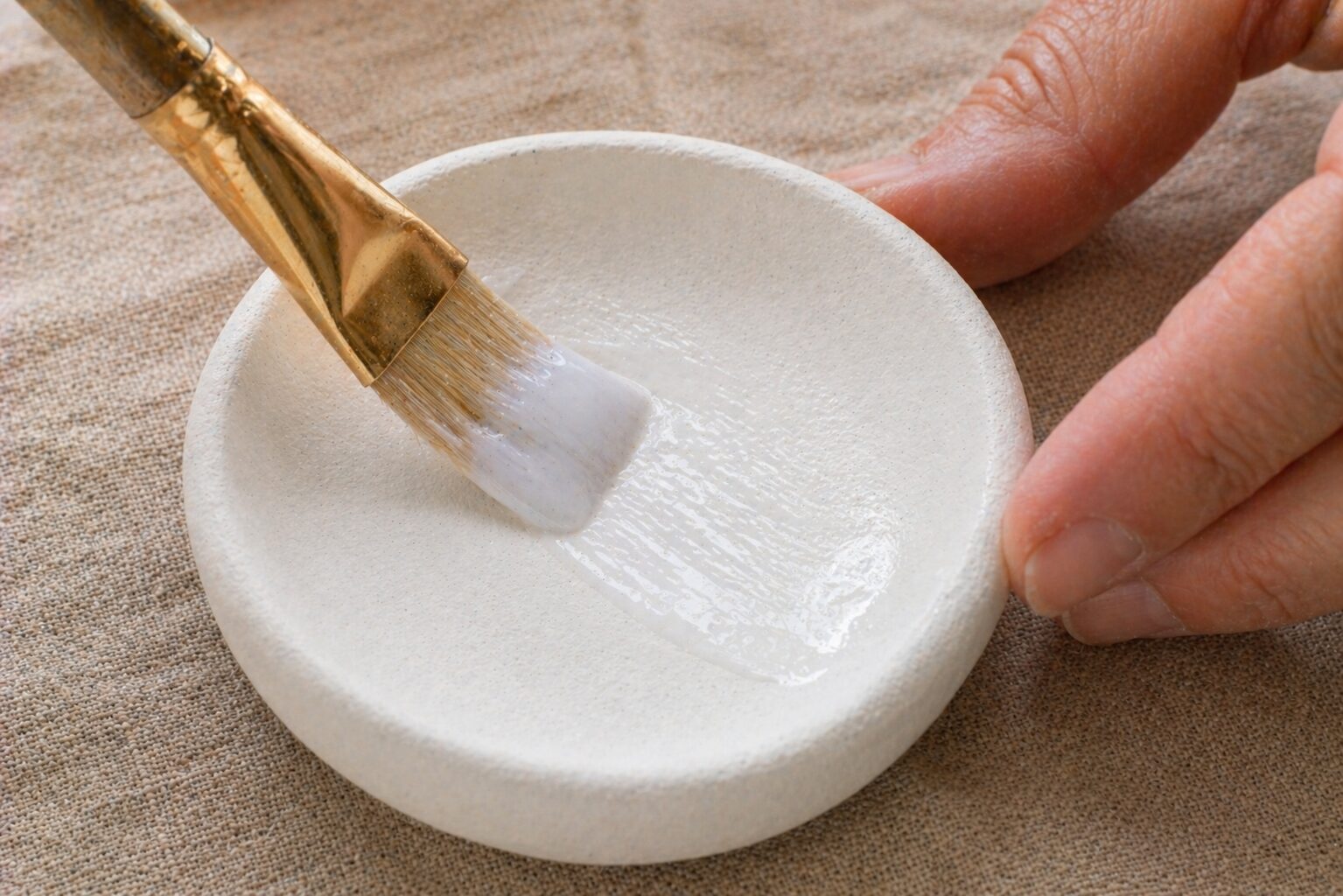 Paintbrush applying a clear Mod Podge sealer coat to the interior of a dried clay dish, showing the milky wet sheen
